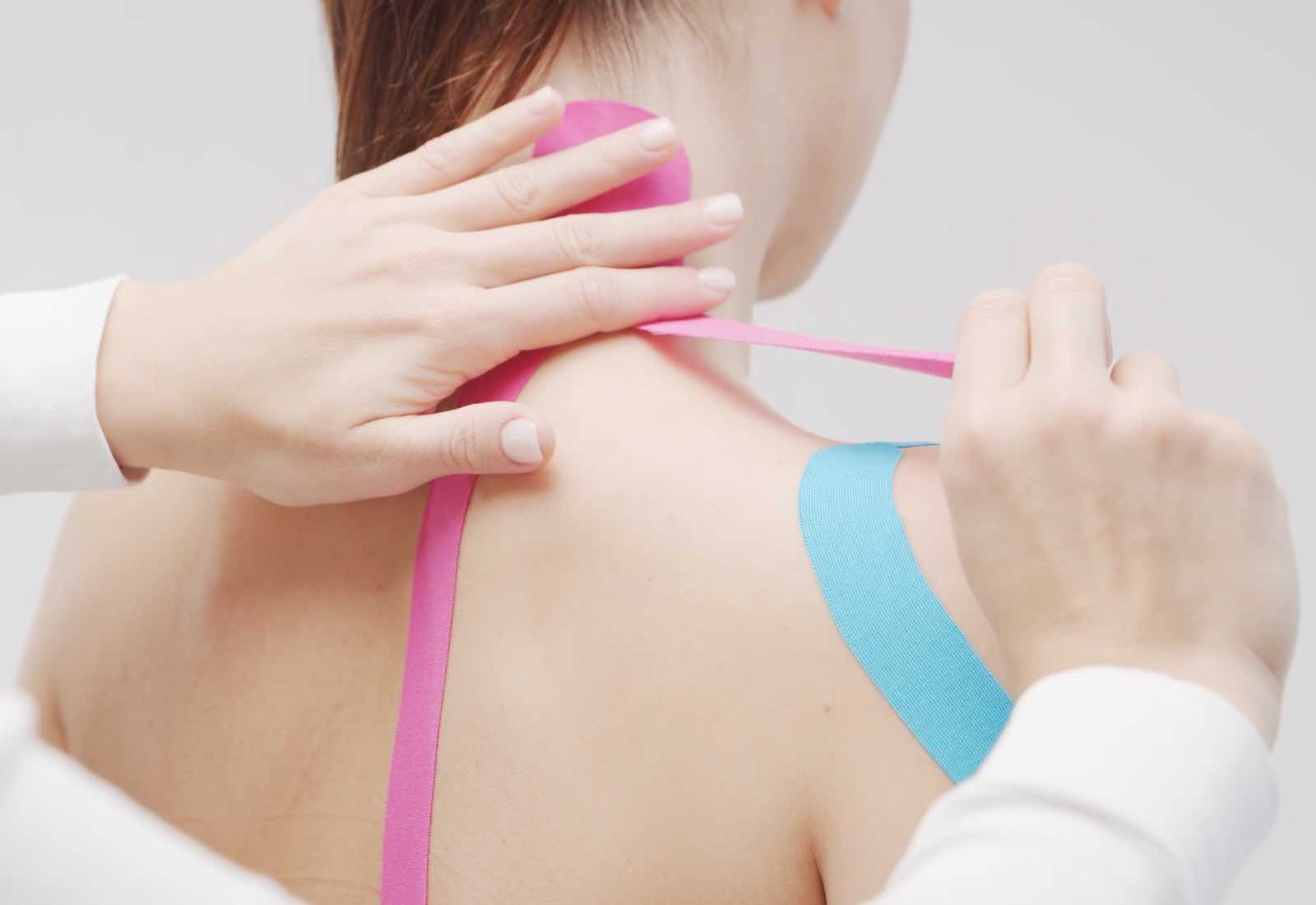 Therapeut bringt kinesiologisches Tape an der Schulter an